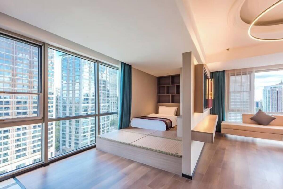 Ein modernes Hotelzimmer mit großem Fenster, einem Bett, einer Couch und einer integrierten Ablagefläche.