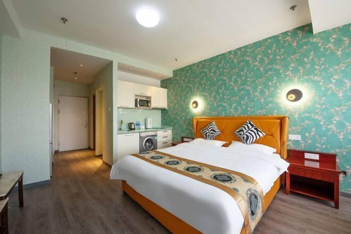 Ein Hotelzimmer mit einem großen Bett, Holzboden, einer Küchenzeile und einem durchgegangenen Tür erkennbaren Badezimmer.