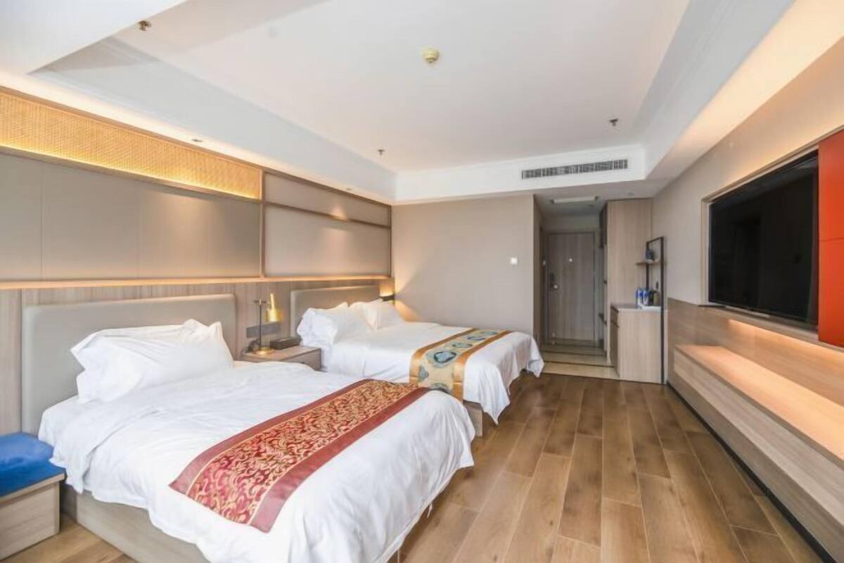 Ein Hotelzimmer mit zwei Betten, einem großen Fernseher und Holzboden.