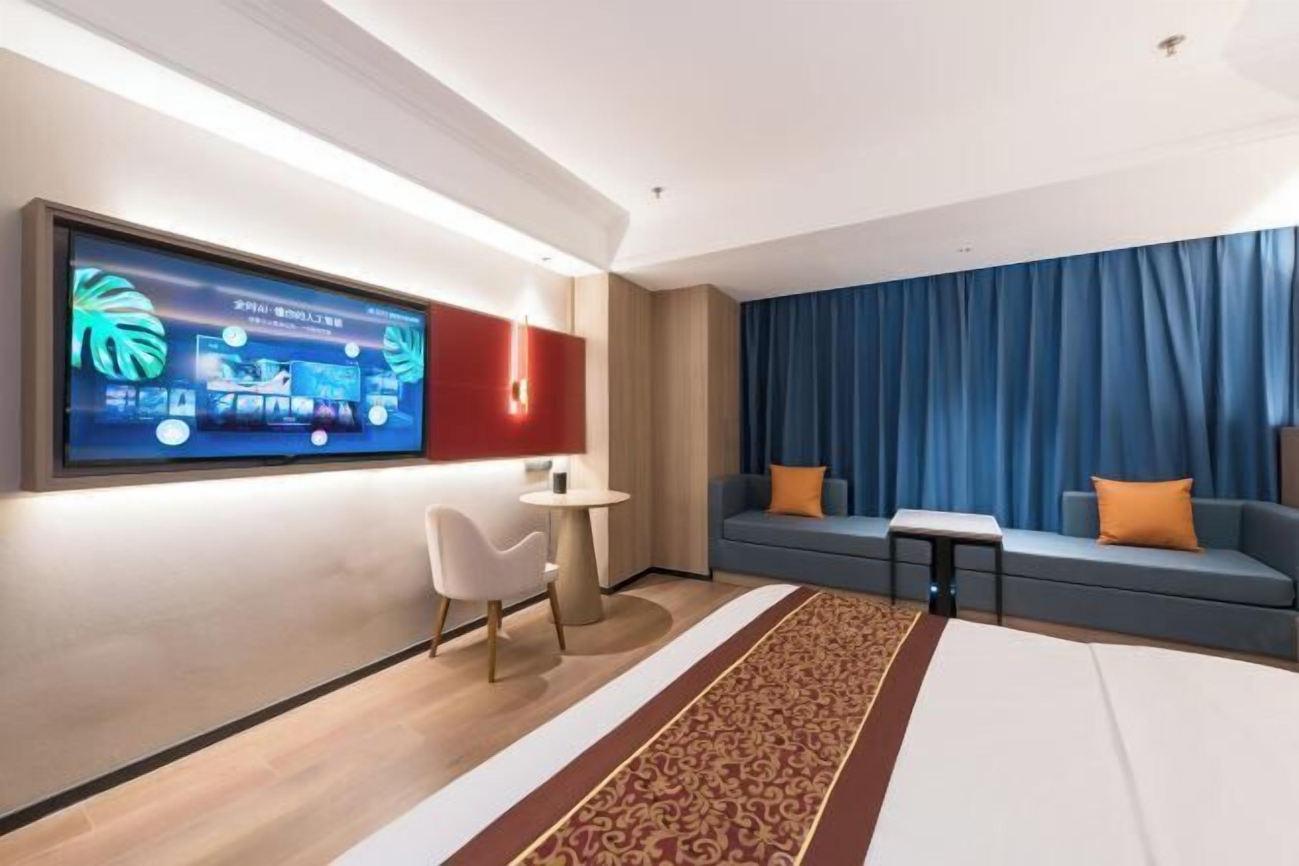 Habitación de hotel moderna con un televisor de pantalla plana grande, un sofá, una mesita y una alfombra estampada.