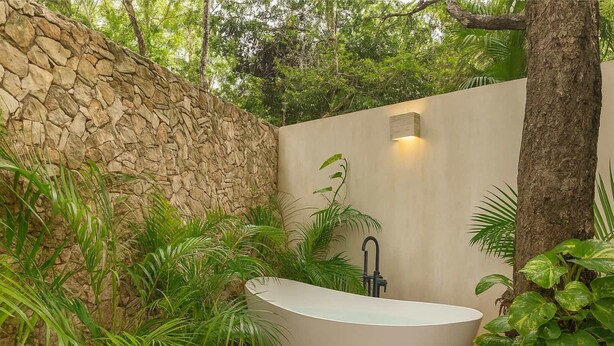 A modern outdoor bathroom with a freestanding bathtub, surrounded by lush greenery and a stone wall. - Aldea Zama Jungle Home: Private Pool & Garden Tub (Tulum)