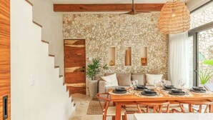 A dining area with a stone wall, wooden staircase, and a hanging light fixture. - Aldea Zama Jungle Home: Private Pool & Garden Tub (Tulum)