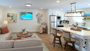 A modern kitchen with white cabinets, a stainless steel refrigerator, and a dining area with a white table and chairs. - 562 Beachy Keen Cottage| New Pool | Mins 2 Beaches (Naples)