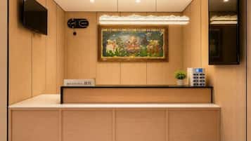 Un mostrador de recepción con un letrero, un cuadro, un reloj y un televisor en la pared.