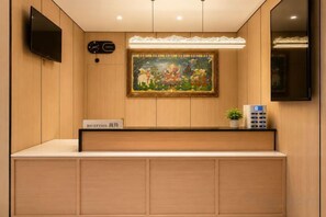 A reception desk with a sign, a painting, a clock, and a television mounted on the wall. - Deji Express Hotel (Maqu)