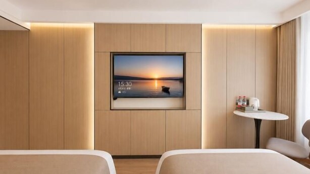 Habitación de hotel con dos camas, un televisor montado en la pared y una mesita con una taza y un libro.