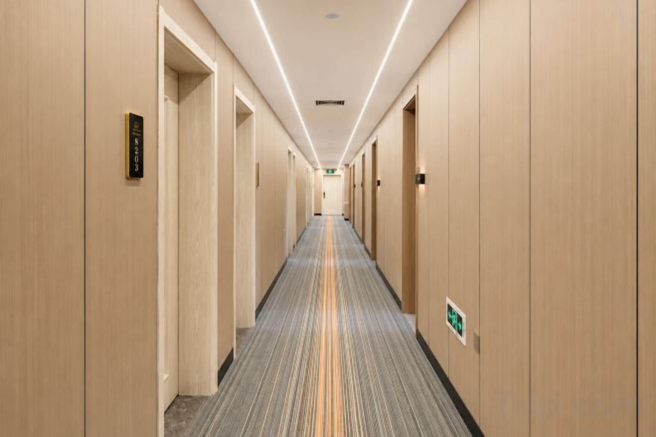 A long, narrow hotel corridor with doors on both sides, carpeted floor, and overhead lighting.