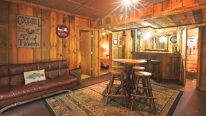 A rustic interior with a wooden bar, a leather sofa, and a patterned rug. - Carriage House Cabin #1 - Near Three Rivers (Walhonding)