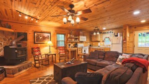 A cozy cabin interior with a stone fireplace, wooden furniture, and a kitchen area. - Carriage House Cabin #1 - Near Three Rivers (Walhonding)