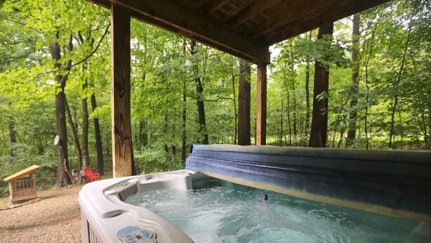 A hot tub in a forested area with a wooden deck and a small wooden structure in the background. - Carriage House Cabin #1 - Near Three Rivers (Walhonding)