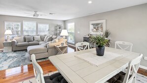 A spacious living room with a large sectional sofa, a dining table, and a ceiling fan. - Delightful 2/2 Beach House LBK 5 Min drive to Beach (Longboat Key)