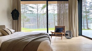 Un dormitorio con una cama grande, una silla y vistas a un lago a través de ventanas de techo a suelo.