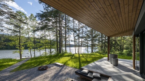 Un espacio de estar moderno al aire libre con vistas a un lago y un bosque.