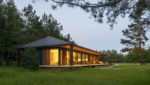 Una casa moderna con amplios ventanales, cimientos de piedra y una terraza de madera.