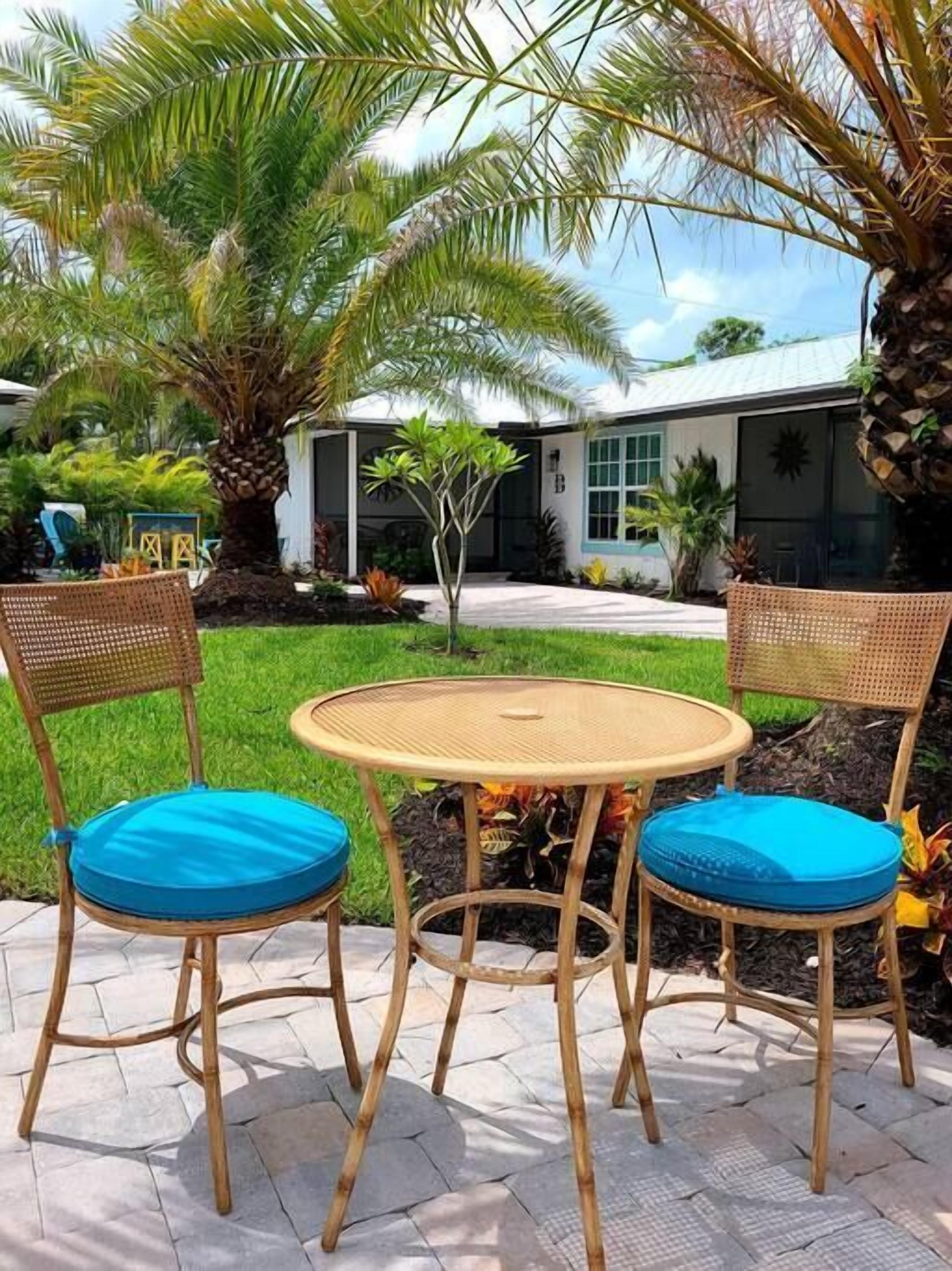 Deux fauteuils en osier avec des coussins bleus, une table ronde en osier et un petit coin jardin agrémenté d’un palmier et d’autres plantes.