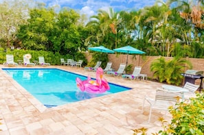 Zona de piscina con sillas de descanso y sombrillas, rodeada de abundante vegetación.