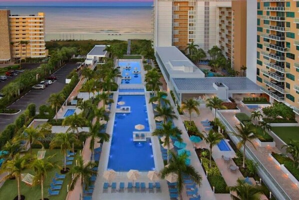 A hotel with a central pool, multiple floors, and a view of the beach.