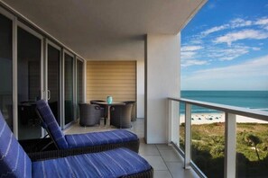 A balcony with a view of the beach, a table with chairs, and a sofa.