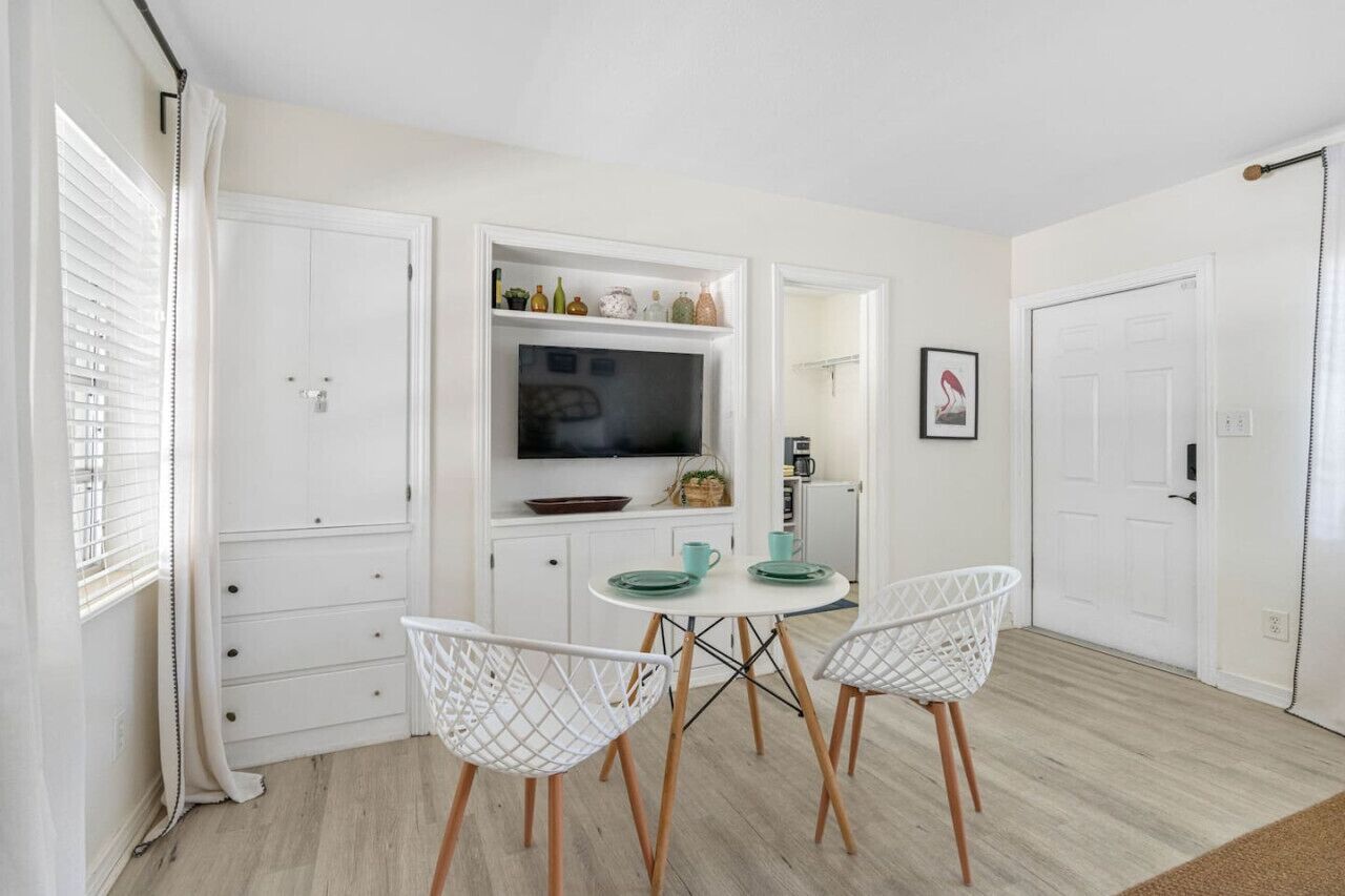 A modern kitchen with white cabinetry, a dining table with white chairs, and a flat-screen TV mounted above the counter.