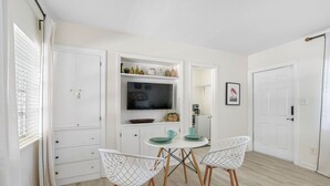 A modern kitchen with white cabinetry, a dining table with white chairs, and a flat-screen TV mounted above the counter. - Perfect Location Vinoy Beach Getaway Sun and fun (St. Petersburg)