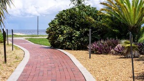 A curved brick pathway leading to a beach with lush greenery and a palm tree. - Perfect Location Vinoy Beach Getaway Sun and fun (St. Petersburg)