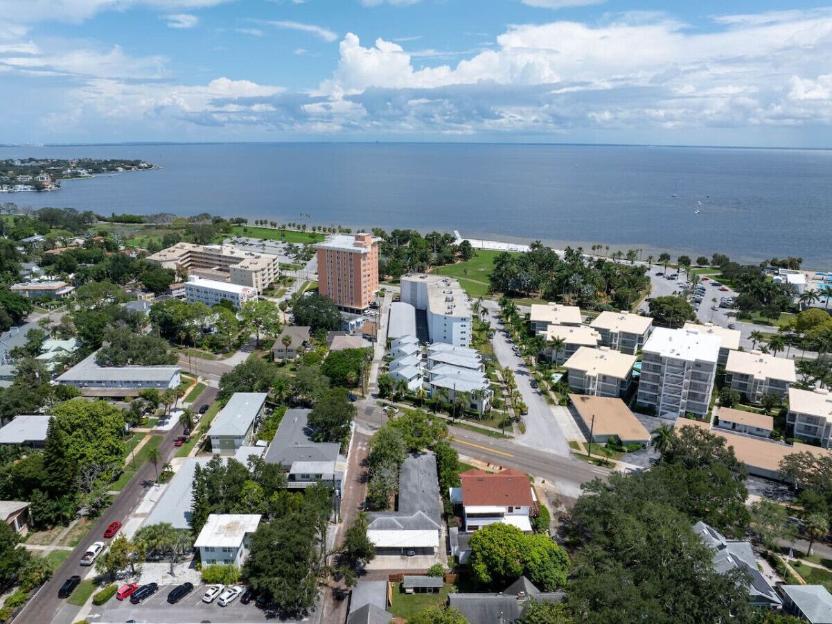 An aerial view of a coastal town with a mix of residential and commercial buildings, a marina, and a large body of water in the background.