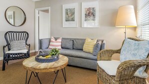 A living room with a grey sofa, a wicker chair, a round wooden coffee table, and a floor lamp. There are two framed artworks on the wall and a mirror above the sofa. - Vinoy Beach getaway, Fun in the Sun Close to bars! (St. Petersburg)