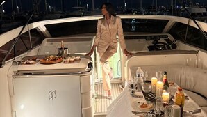 Eine Yacht mit Essbereich auf dem Deck, eine Person steht am Tisch, im Hintergrund ein Hafen.