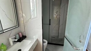 A bathroom with a white sink, a mirror, a toilet, and a glass shower enclosure. - Shijixing Business Hotel (Baoying)
