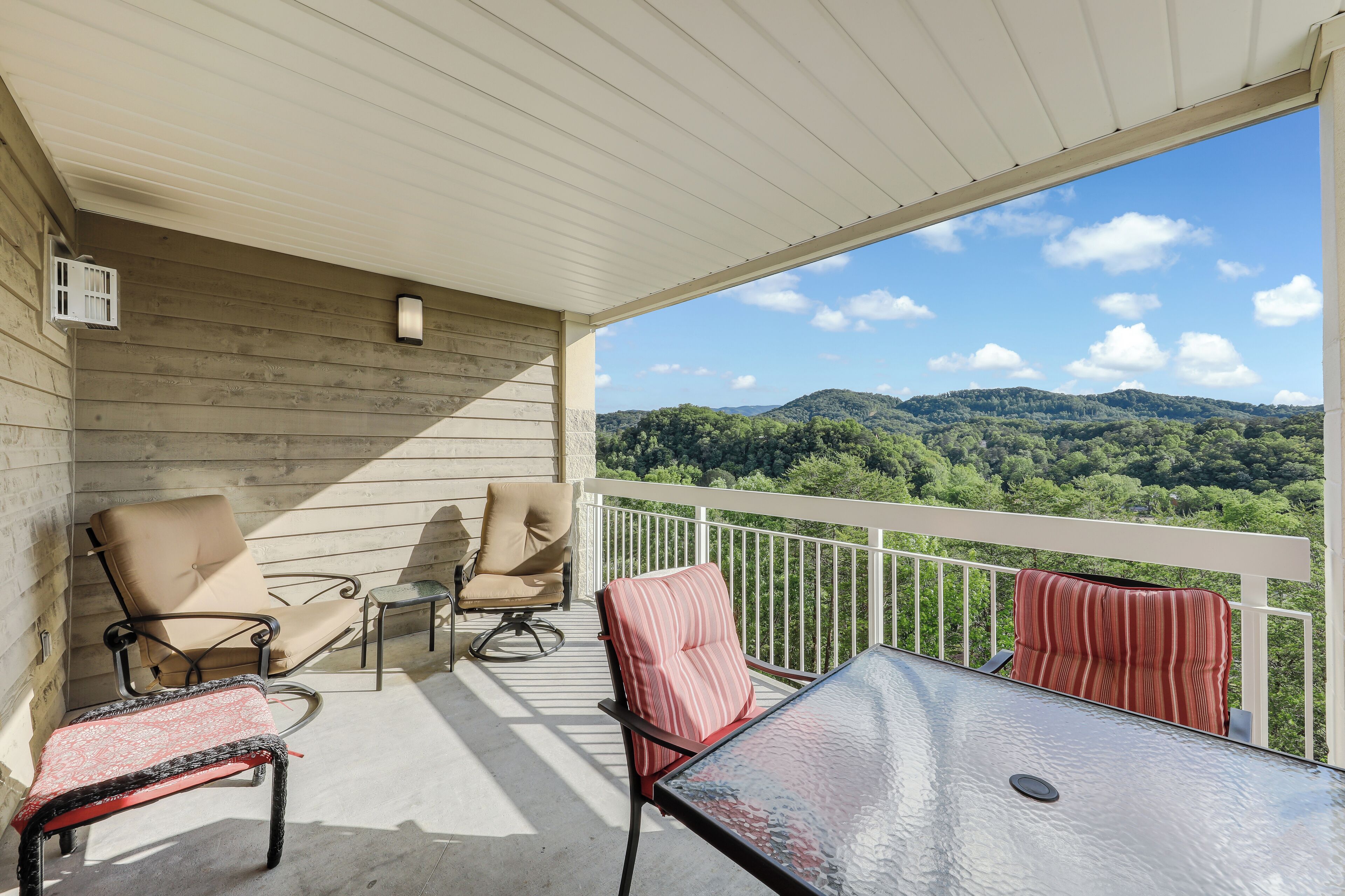 A balcony with a view of green hills, a glass table, and two chairs.
