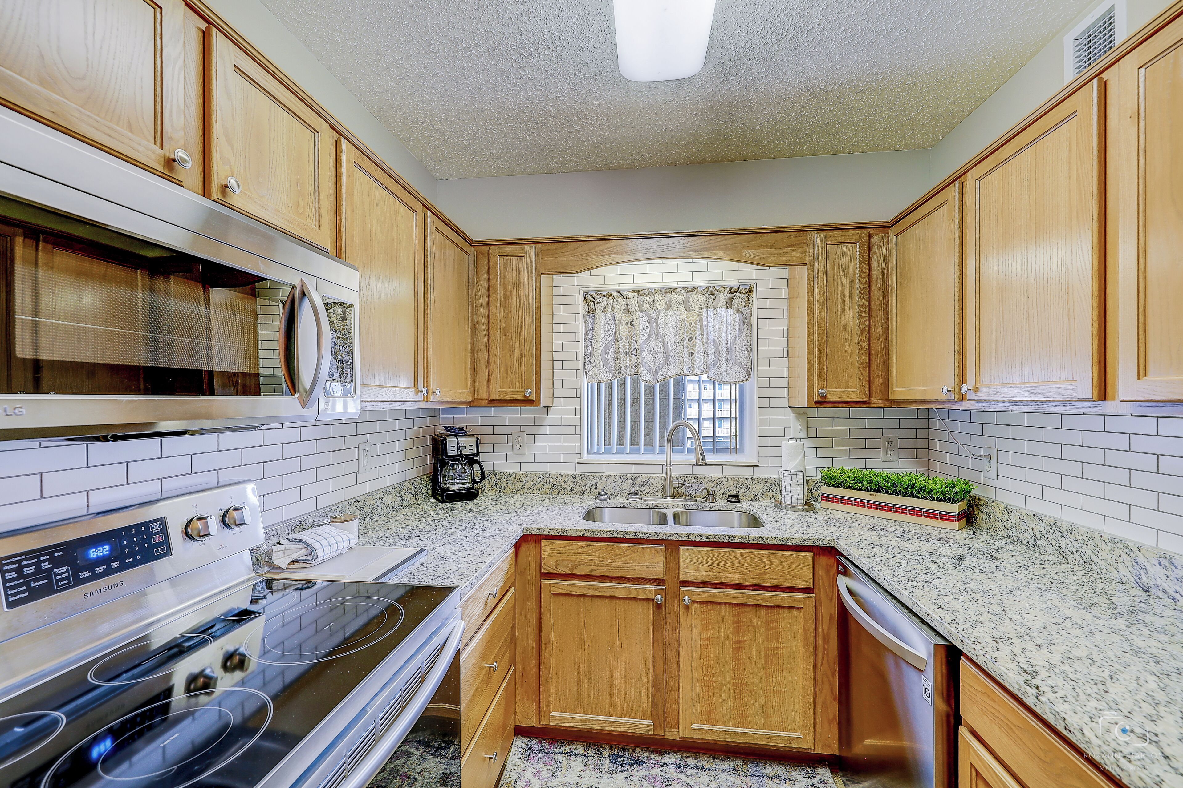 A kitchen with wooden cabinets, a stainless steel stove, a microwave, and a sink with a window above it.