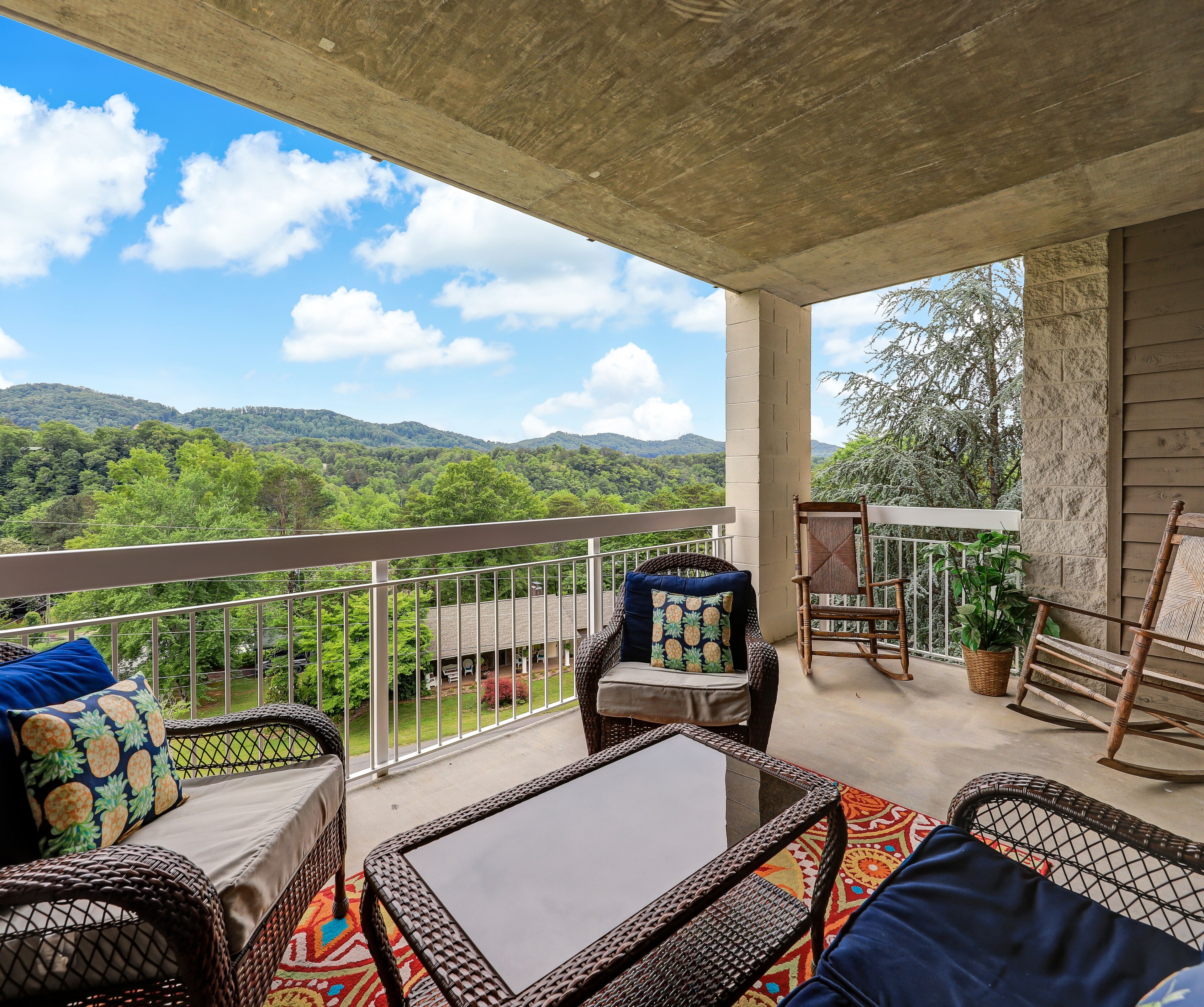 A balcony with wicker furniture, a view of green hills, and a clear sky.