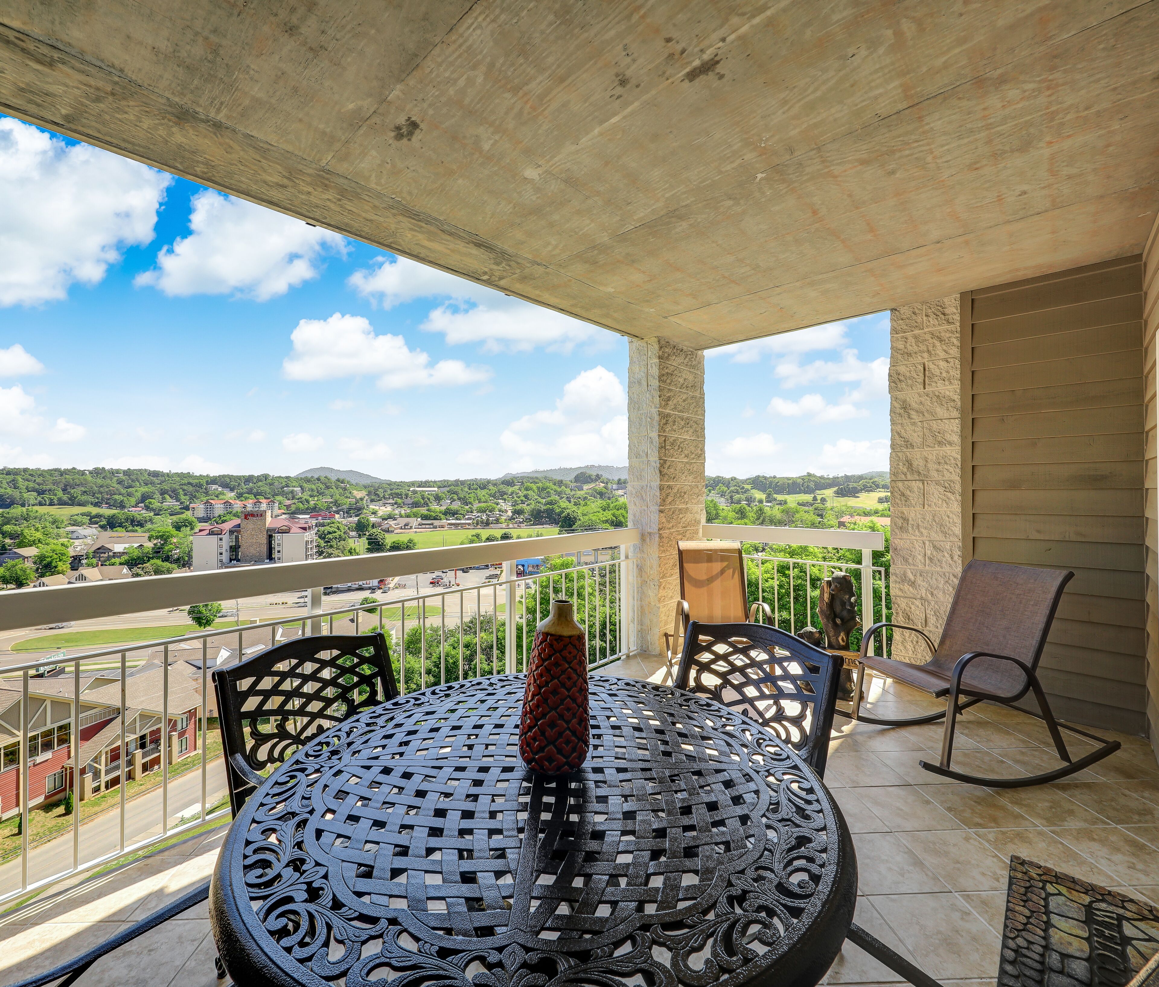 A balcony with a round metal table, chairs, and a decorative vase.