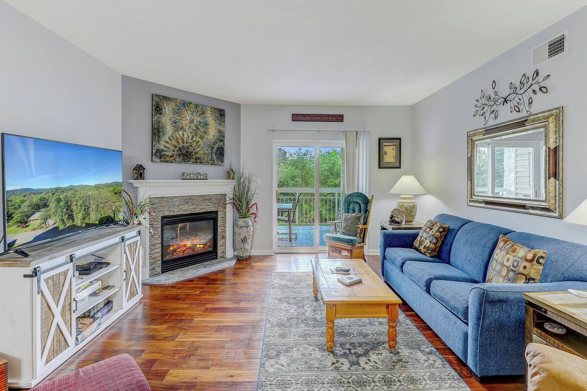 Una sala de estar con chimenea, televisor, sofá y vistas al exterior.