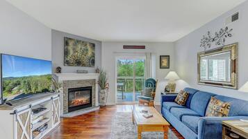A living room with a fireplace, a television, a sofa, and a view of the outdoors.