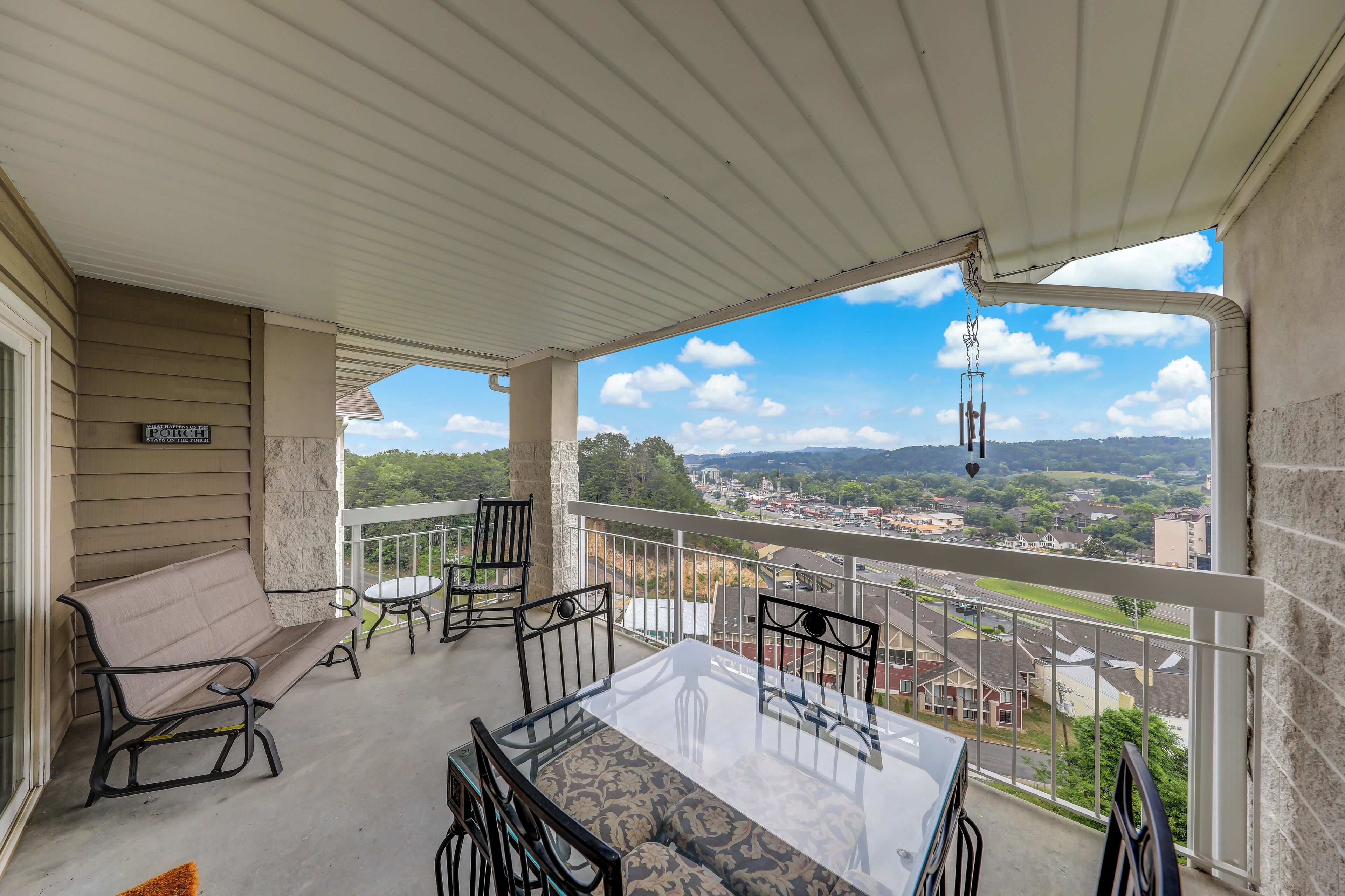 A balcony with a table and chairs, a bench, and a view of a town and mountains.