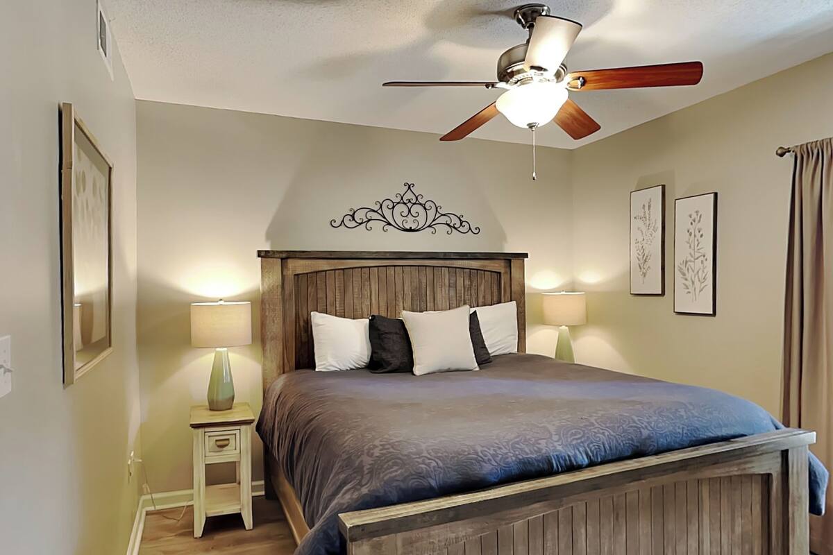 Un dormitorio con estructura de cama de madera, un ventilador de techo y dos lámparas de noche.