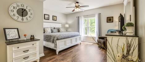 A bedroom with a bed, a dresser, a clock, a ceiling fan, and a window with curtains.
