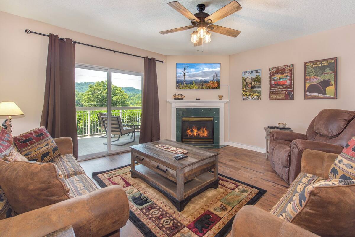 Una sala de estar con chimenea, ventilador de techo y balcón con vistas a la vegetación.
