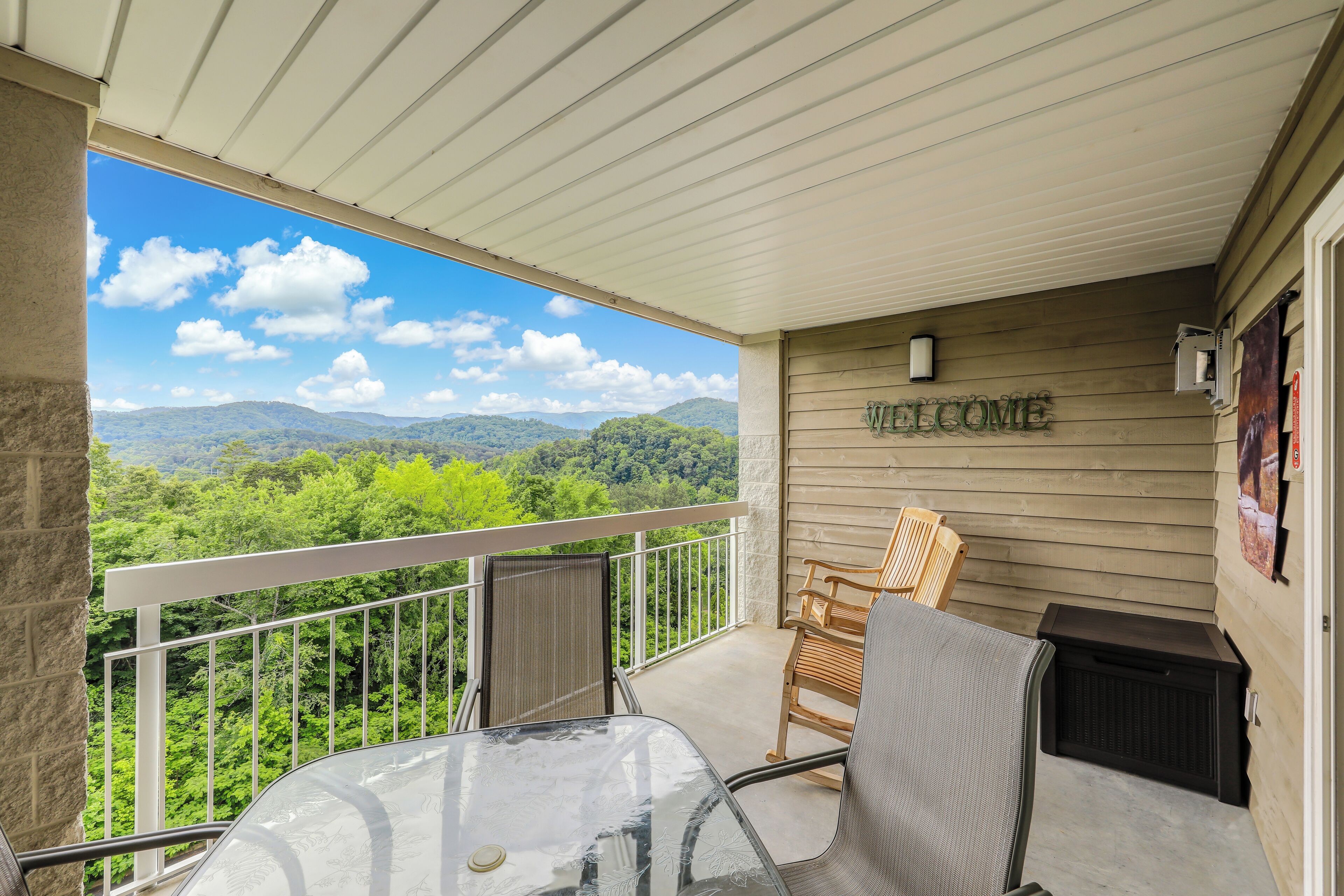 A balcony with a view of mountains, a welcome sign, and a table with chairs.