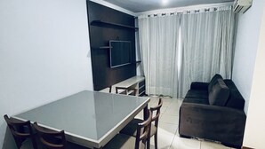 A dining area with a table and chairs, a TV mounted on the wall, a sofa, and a window with curtains. - Great 2 Bedroom Apartment - Excellent Location (Cuiabá)