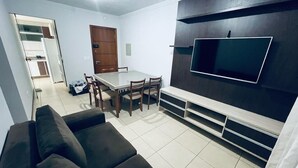 A modern living room with a dark-colored sofa, a dining table with chairs, and a flat-screen TV mounted on a dark wall. - Great 2 Bedroom Apartment - Excellent Location (Cuiabá)