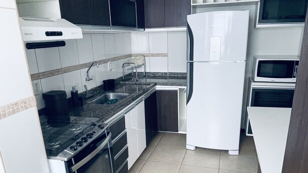 A compact kitchen with a stove, sink, and white refrigerator. - Great 2 Bedroom Apartment - Excellent Location (Cuiabá)