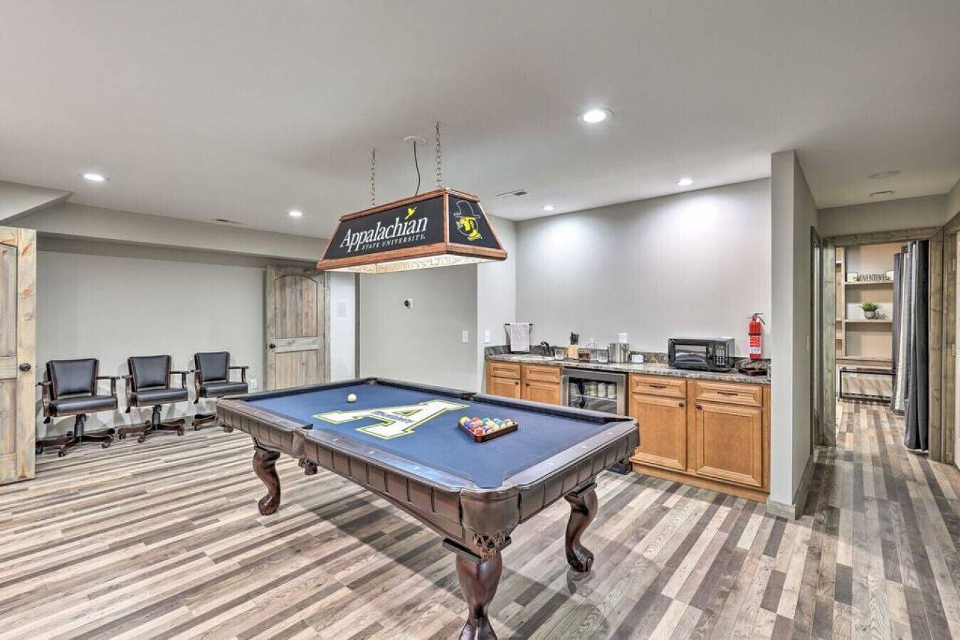 A pool table with a sign above it, a kitchen area, and a seating area with chairs.