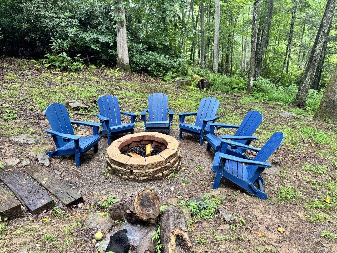 A circular seating arrangement with chairs around a central fire pit in a forest setting.