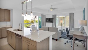 Una cocina moderna con una isla central, un área de comedor con mesa y sillas, un sofá y un televisor montado en la pared.