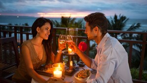 Una pareja cenando en una mesa con una vela y una copa de vino, con vistas a un paisaje marino.