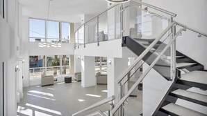 Un interior moderno con una escalera de cristal, ventanas amplias y un techo alto.