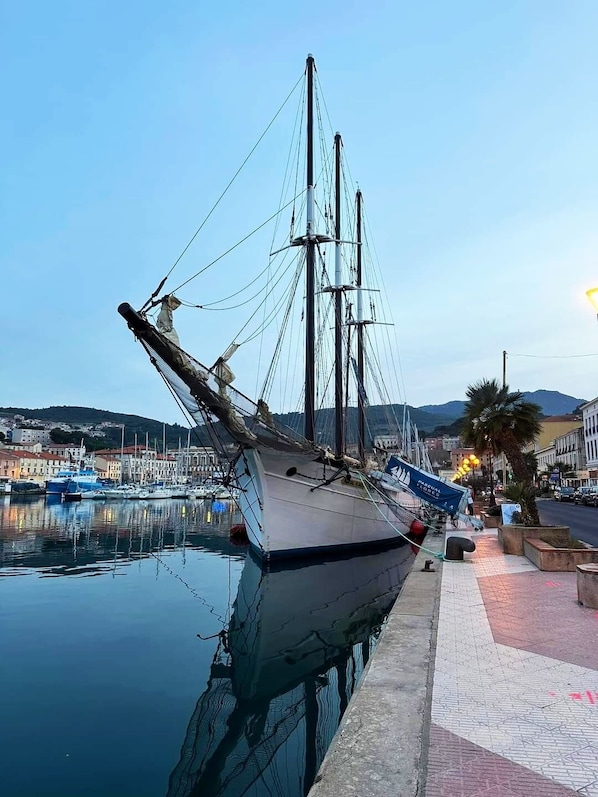 Un alto barco velero amarrado en un puerto deportivo, con un paisaje urbano al fondo.