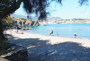 A beach with people sunbathing and swimming, rocky terrain, and a clear view of the water.
